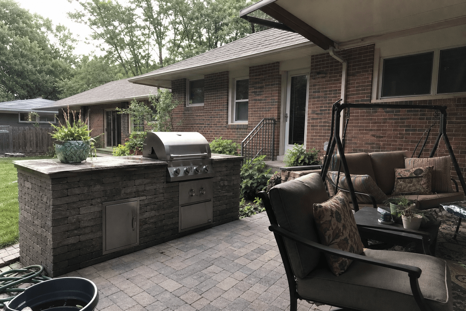 Outdoor kitchen and stone patio area beside a brick home.